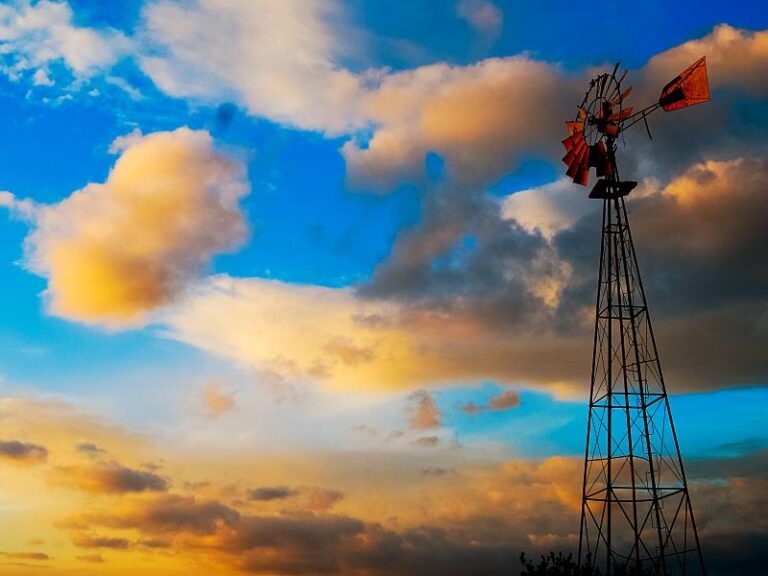 Paisaje al atardecer de cielo con nubes y a la derecha de la imagen la molineta destartalada para sacar agua de un pozo.