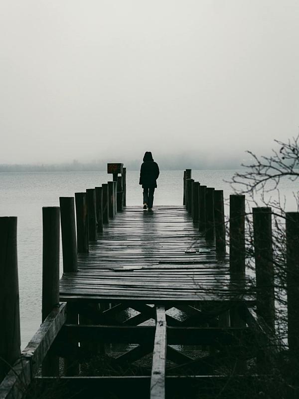 Persona andando en un muelle junto al agua. Imagen en blanco y negro