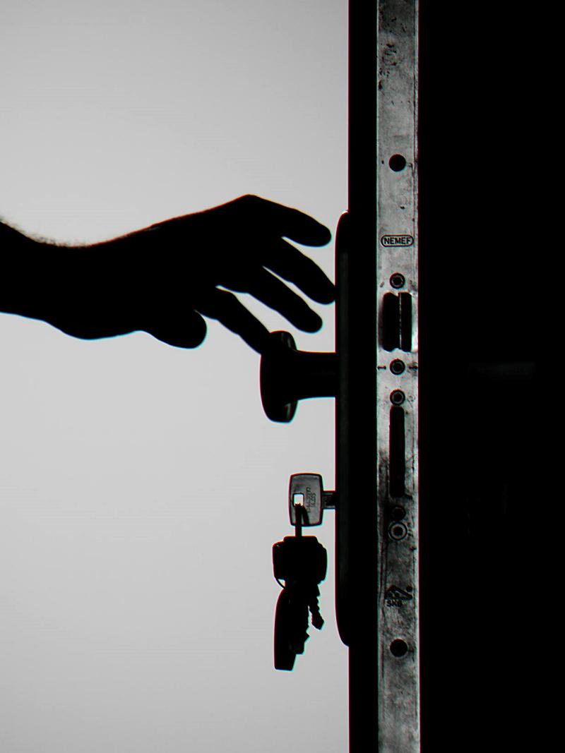 Mano de una persona en el picaporte de una puerta. Se ven las llaves puestas en la cerradura. En blanco y negro.