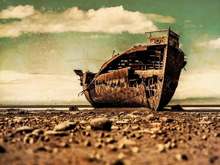 Cascarón de barco en estado ruinoso varado en lo que parece un desierto con un charco de agua