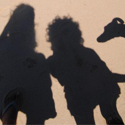 Sombras sobre la arena de playa de dos personas y un perro