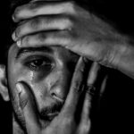 Hombre joven se sujeta la cabeza y se abre el ojo derecho mientras llora.