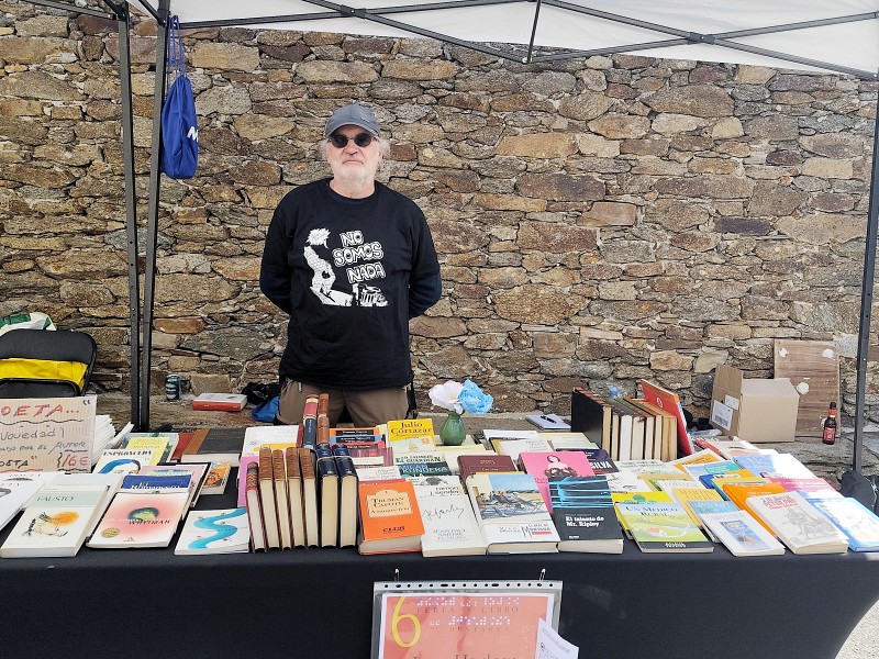 Mesa de puesto en la Feria del Libro de Bustares. Se ven varios libros en la mesa puestos a la venta. Tras la mesa el regente de la librería Jean Harlos, Javier del Sastre.