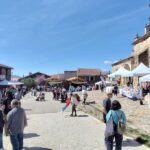 Calle Mayor de Bustares en el día de la VI Feria del Libro. Se ve la calle con gente y los puestos participantes. A la derecha se ve la iglesia de San Lorenzo.