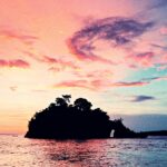 Silueta de una isla se ve en el horizonte en el mar con el cielo con nubes en el atardecer.