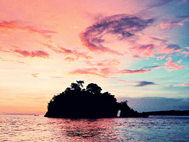 Silueta de una isla se ve en el horizonte en el mar con el cielo con nubes en el atardecer.
