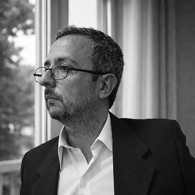 Perfil Meneghetti. Hombre con gafas, moreno y chaqueta negra con camisa blanca. Foto retrato en blanco y negro.